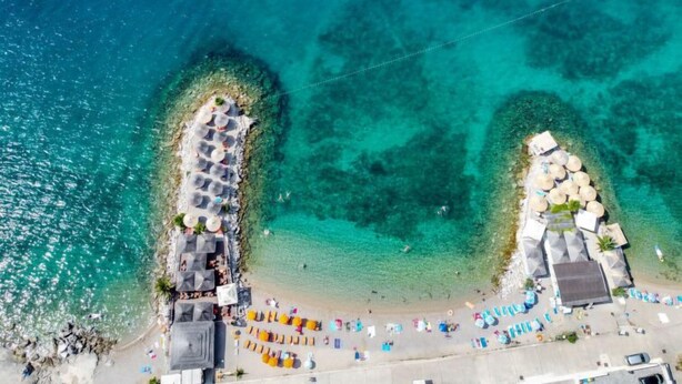 An aerial view of a beach with clear turquoise waters, a sandy shore, and a series of sun loungers and umbrellas arranged along the beach. - Vacation home Vesna by Interhome (Krk/Njivice)