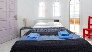 A bedroom with a bed, two windows, a nightstand, a lamp, and a red chair. - Bella Vista by Interhome (Calonge)