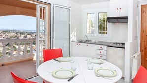 A balcony with a table set for two, a kitchen with white cabinets and red handles, and a view of the city. - Bella Vista by Interhome (Calonge)
