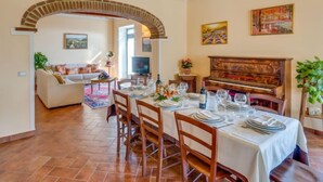 A dining area with a wooden table set for six, a piano, and a TV in the background. - Vacation home Zen by Interhome (Castiglion Fiorentino)