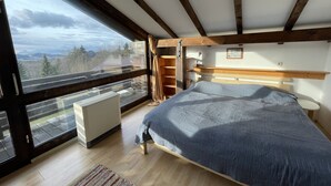 A bedroom with a large bed, wooden beams, a view through a window, and a radiator. - Ferienpark Vorauf by Interhome (Siegsdorf)