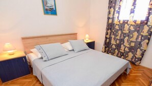Una cama bien hecha con una colcha a rayas y almohadones, flanqueada por mesitas de noche con lámparas, en una habitación con suelo de parquet de madera y cortinas estampadas.