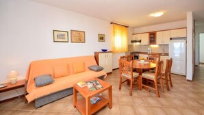 Un espacio habitable compacto con sofá, mesa de comedor, sillas, una pequeña cocina y suelo de baldosas.