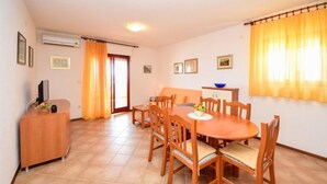 Un comedor con una mesa de madera redonda y sillas, una mesita auxiliar con un cuenco, y un sofá al fondo.