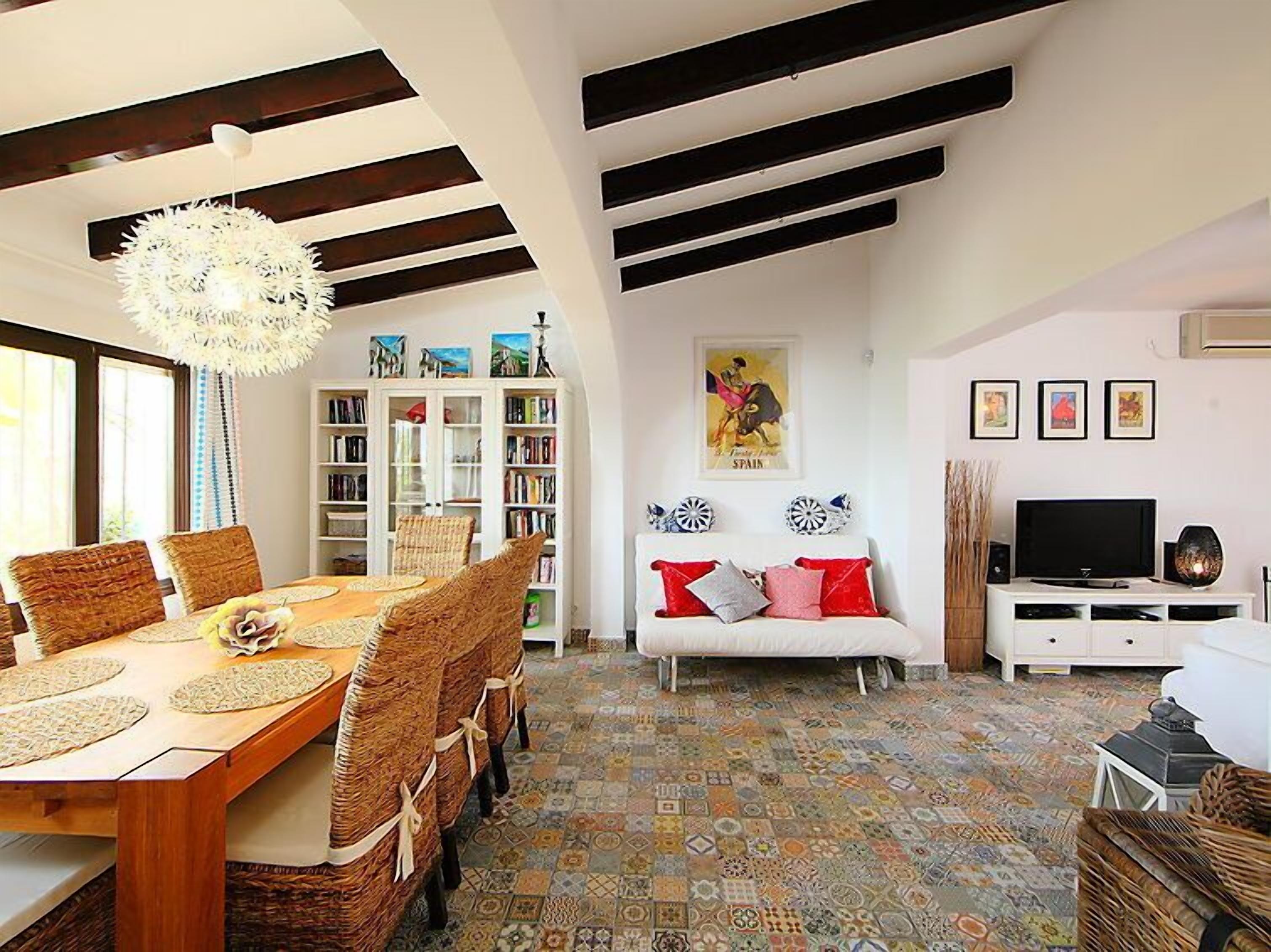 A living room with a dining table, chairs, a sofa, a bookshelf, a television, and a patterned floor.