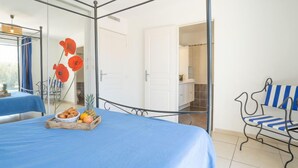 A bedroom with a four-poster bed, a small table with fruit, and a chair with striped cushions. - Les Villas de l'Etang by Interhome (Canet-Plage)