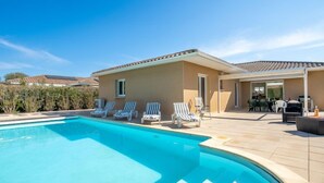 A swimming pool with lounge chairs, a patio area, and a building with a tiled roof. - Les Villas de l'Etang by Interhome (Canet-Plage)