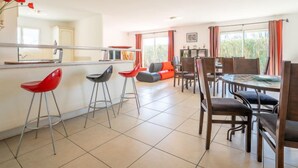 A modern kitchen with a bar area, a dining area with wooden chairs, and a living space with a sofa and red chairs. - Les Villas de l'Etang by Interhome (Canet-Plage)