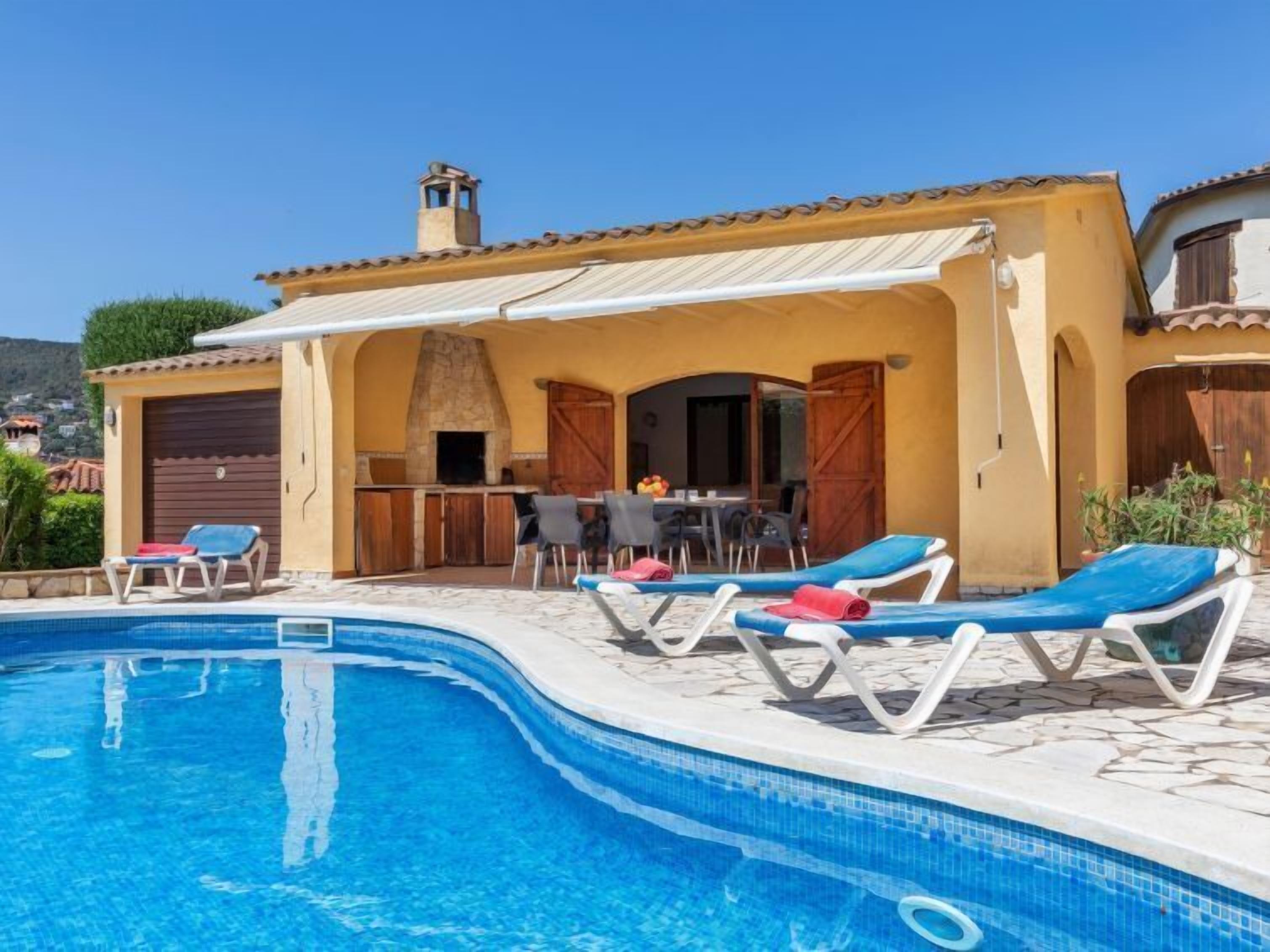 A swimming pool with lounge chairs, a barbecue area, and a view of the surrounding landscape.