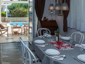 Un coin repas avec une table mise pour le dîner, une bouteille de vin et une vue sur une piscine.