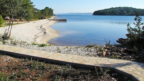 Ein Strand mit einem Kiesweg, der zum Wasser führt, umgeben von Bäumen und einer entfernten Insel.