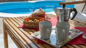 Ein Holztisch mit Tablett, zwei Tassen, einem Obstkorb und einer Kaffeekanne am Pool.