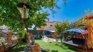 Een binnenplaats met een stenen fontein, een bankje en een pergola met een blauwe parasol.