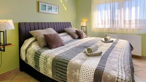 Een slaapkamer met een bed, kussens, een deken, een lamp en een raam met gordijnen.