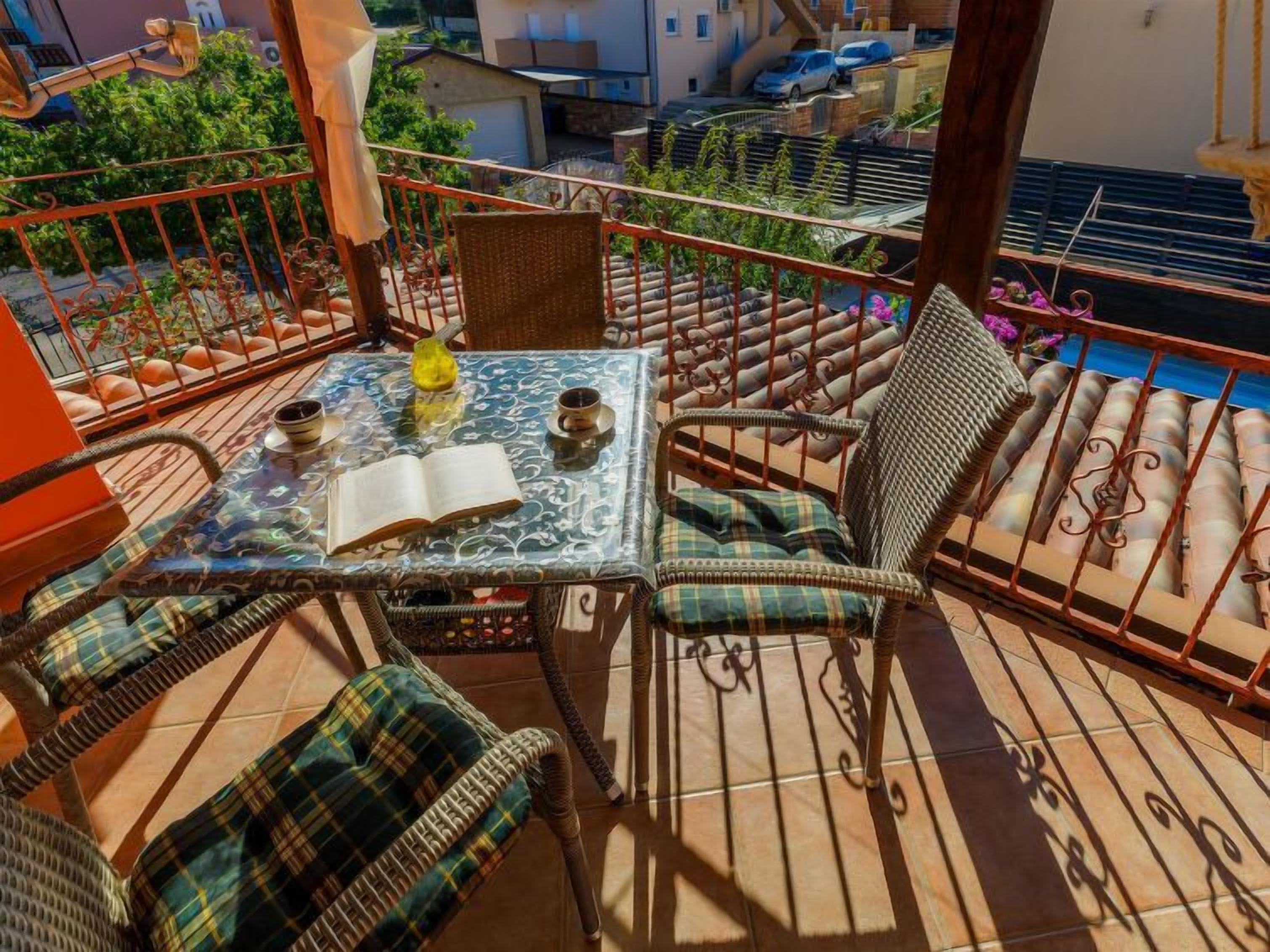 Un balcón con una mesa de vidrio, sillas de mimbre y un libro.