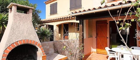 A two-story house with a brick oven and a patio with a table and chairs.
