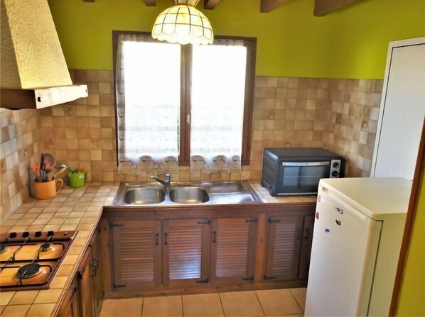 A kitchen with a gas stove, two sinks, a microwave, and a refrigerator.