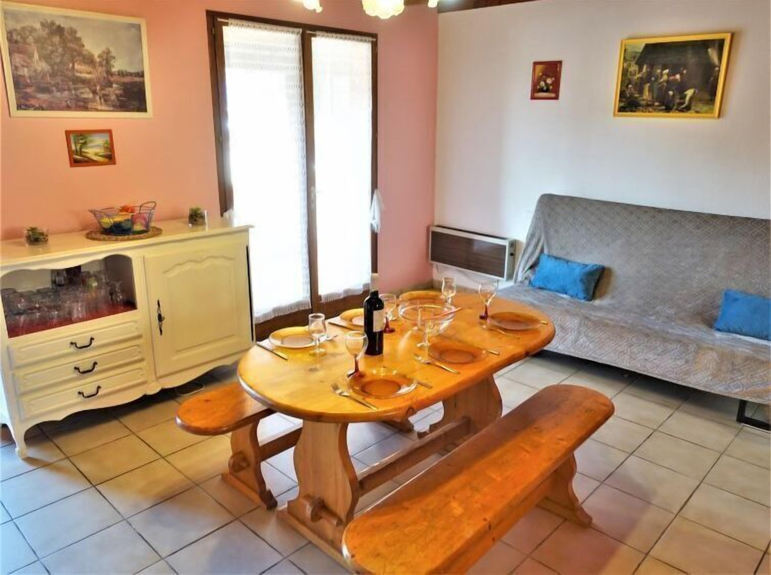 Un coin repas avec une table en bois dressée pour quatre personnes, un buffet blanc contenant de la verrerie, un canapé avec des coussins bleus et un tableau accroché au mur.