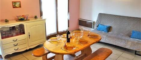 Un coin repas avec une table en bois dressée pour quatre personnes, un buffet blanc contenant de la verrerie, un canapé avec des coussins bleus et un tableau accroché au mur.