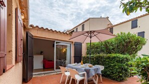 Patio esterno con tavolo e sedie, una porta scorrevole in vetro che dà su una stanza e un'area riparata con un ombrellone.