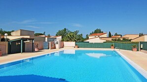 Una piscina cristallina circondata da un'area recintata, con una zona relax coperta e un edificio con tetto rosso.