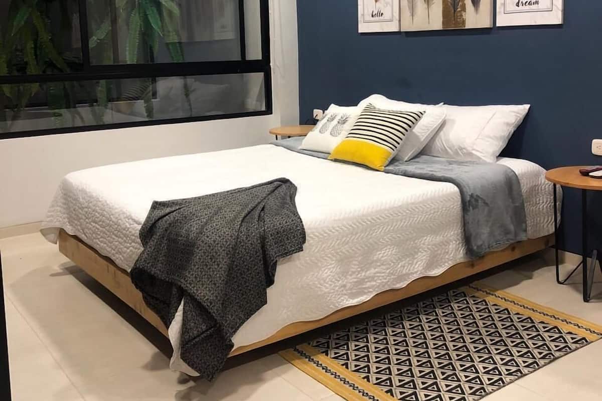 Une chambre moderne avec un grand lit, une petite table de chevet, une fenêtre donnant sur un paysage verdoyant et des œuvres d’art murales.