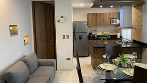 A modern kitchen with a refrigerator, microwave, and stove. There is a dining table with chairs and a sofa in the living area. - Kapital Suites (Pereira)