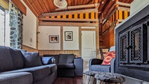 Ein gemütliches Wohnzimmer mit Holzbalkendecke, einem Kamin und einer Treppe, die in ein Obergeschoss führt.