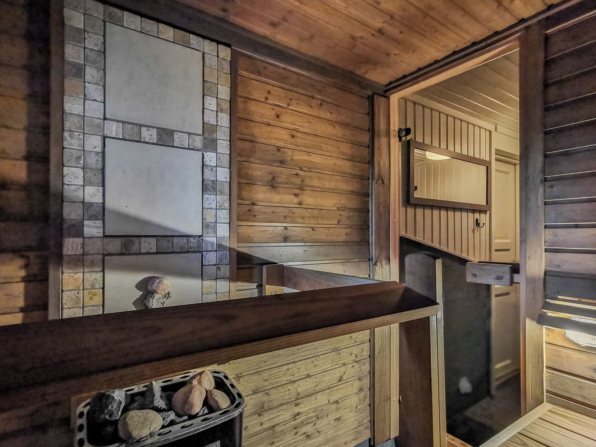 A wooden interior with a stone wall, a wooden bench, and a fireplace with logs.