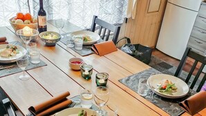 Ein Esstisch ist gedeckt mit Tellern, Gläsern und einer Weinflasche, umgeben von Stühlen und einem gemusterten Vorhang im Hintergrund.