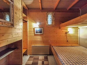 Una camera in un rifugio di legno con un letto, un termosifone, un quadro appeso al muro e uno specchio.