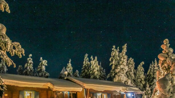 Eine Holzhütte mit verschneietem Dach, einer Holzwand und einer Veranda mit Geländer.