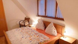 Une chambre à coucher avec un lit, des oreillers, une chaise, une table de chevet et une fenêtre avec des rideaux.