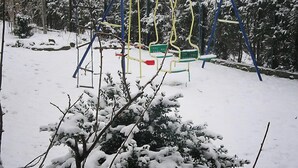 Un espace extérieur enneigé, équipé d’une balançoire et de bancs.