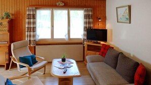 A living room with a wooden floor, a sofa, two armchairs, a coffee table, a TV, and a window with curtains. - Untertal by Interhome (Elm)