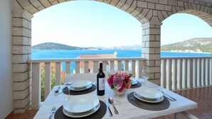 Une table dressée pour deux personnes, avec une bouteille de vin et un vase de fleurs, donnant sur une vue panoramique de la côte.