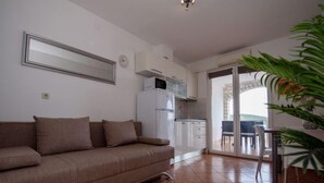 Un salon comprenant un canapé, un coin cuisine et une porte-fenêtre coulissante donnant sur un balcon.