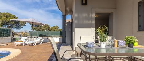 An outdoor patio with a pool, lounge chairs, and a table set for dining.