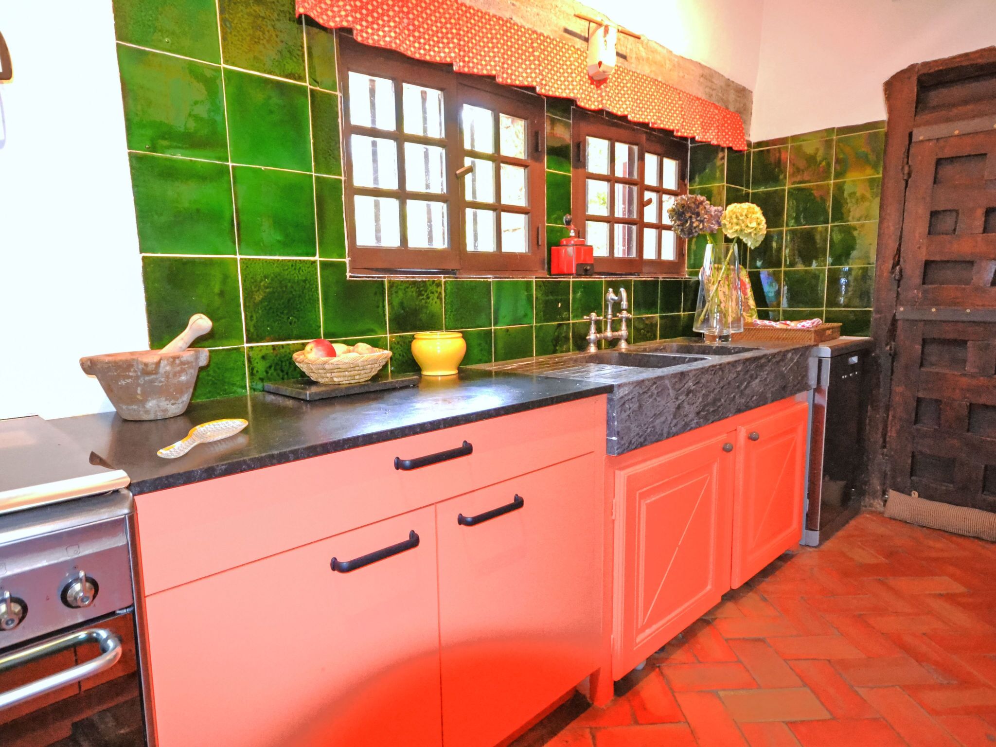 Een keuken met groene tegels, een rode spoelbak en een houten deur.