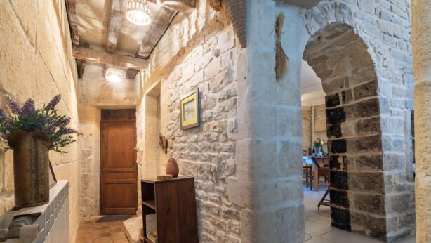 Un pasillo de paredes de piedra con una puerta de madera, un radiador y una planta.