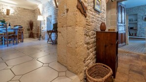 Un interior rústico con paredes de piedra vista, una mesa de madera para comer y suelo de baldosas hexagonales.