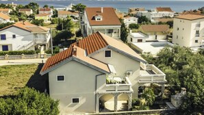 Zona residencial amb cases que tenen teulades vermelles i parets de colors clares, envoltada de vegetació i una vista al mar.