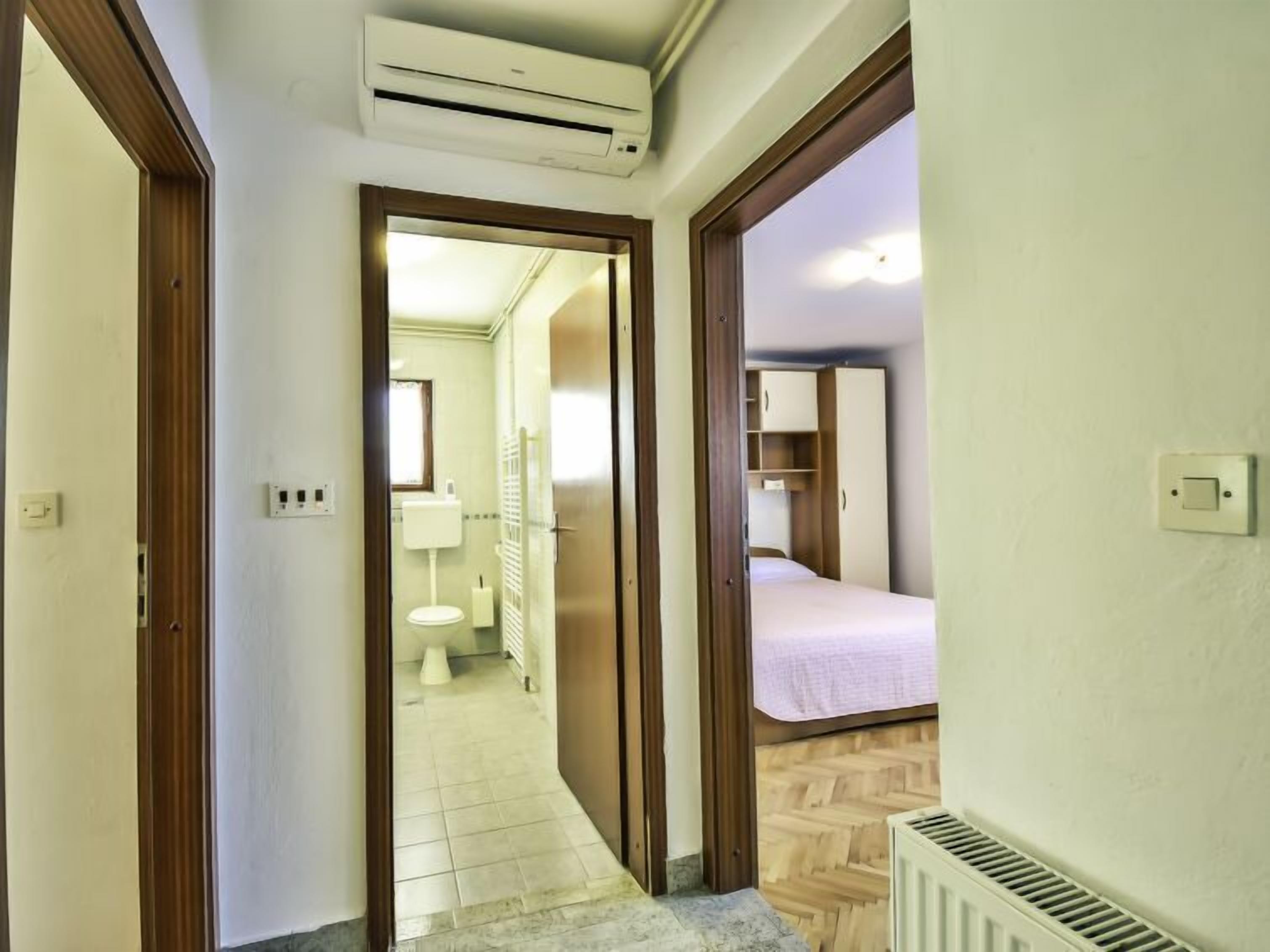 A narrow hallway leading to a bedroom with a bed, a radiator, and a window.