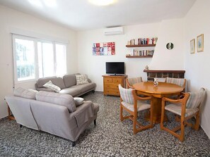 Una sala de estar con sofá, televisor, mesa de centro y sillas. Hay estanterías y una chimenea.
