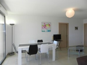 Una sala de estar moderna con una mesa de comedor, sillas, un televisor y una mesa de centro de vidrio.
