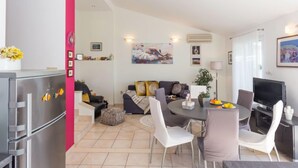 A modern living room with a dining area, a kitchen with a refrigerator, and a TV.