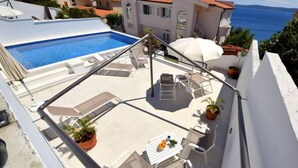 A rooftop terrace with a swimming pool, lounge chairs, and a table with fruit.