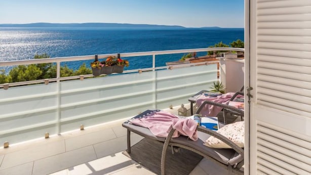 A balcony with a view of the sea, a chair, a table with a towel, and a flower pot.