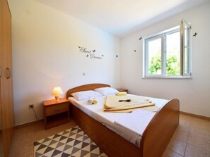 A bedroom with a bed, a nightstand, a lamp, a window, and a wall decoration.