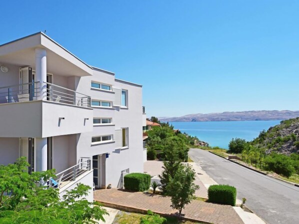 A modern two-story building with balconies, a paved driveway, and a view of a lake.